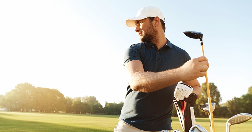 Focused young man golfer taking out the golf club from a bag while standing on a field