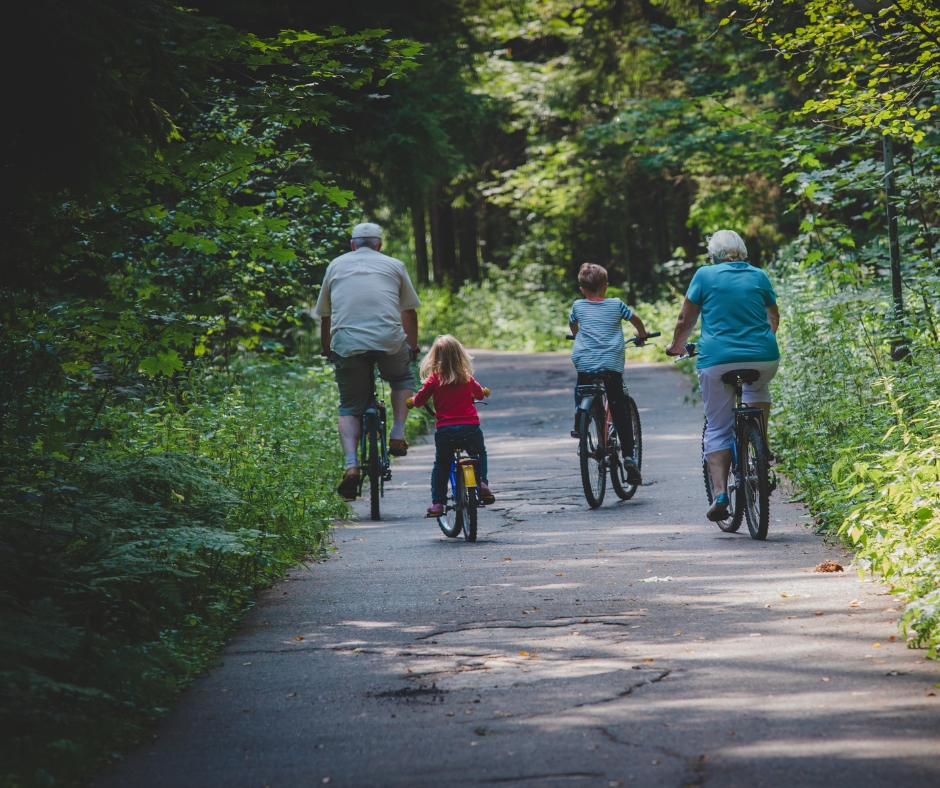 Family of children with grandparents having fun cycling through the woods