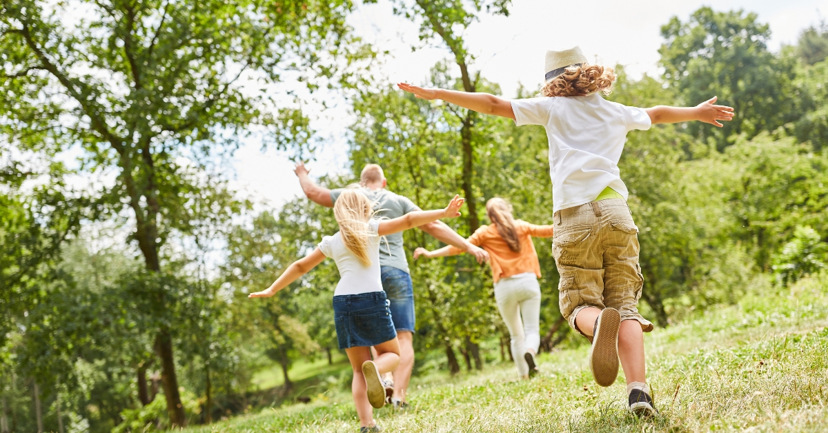 Children and their father frolicking on the grass and trees 