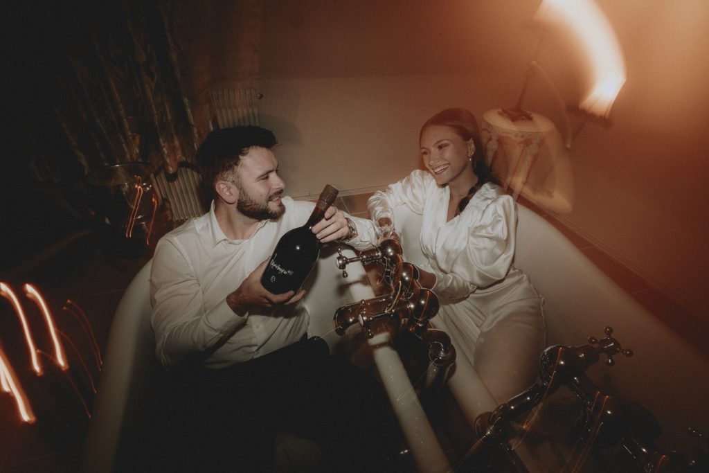 Couple pose in the evening surrounded by candles in the honeymoon suite in the romantic twin bath tubs